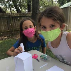 Two kids build an engineering project with papers, tape, scissors and glue