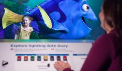 Un adulto y un niño interactúan con una exhibición de Pixar con un pez azul de dibujos animados