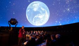An audience looks up at a view of the earth from space, projected on a planetarium dome