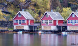 Three identical houses with peaked roofs float on a lake with a mountain behind them.