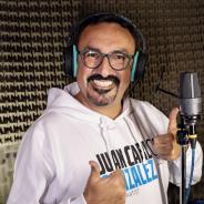 An Ecuadorian man wearing headphones and glasses standing in front of a microphone. Juan Carlos has a mustache and goatee. He is smiling at the camera and giving a thumbs up sign.