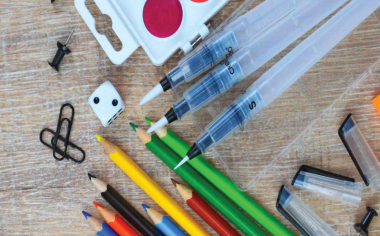 Art supplies on a desk: paints, paperclips, colored pencils and dice